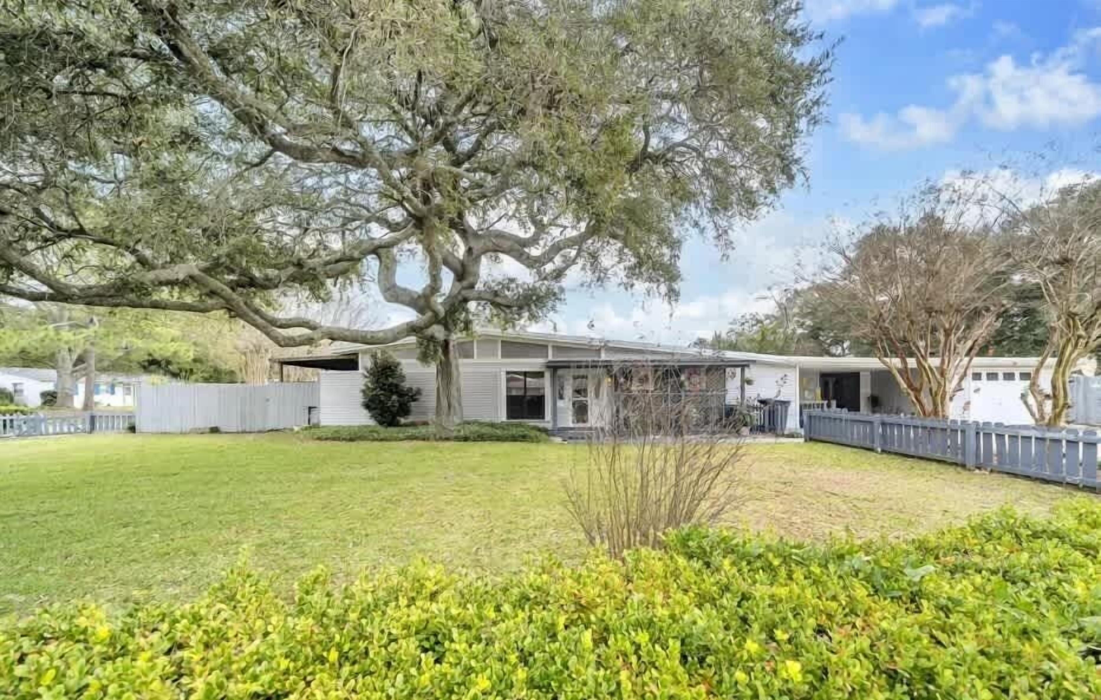 A house with a large tree in the front yard, a fenced yard, and a clear sky.