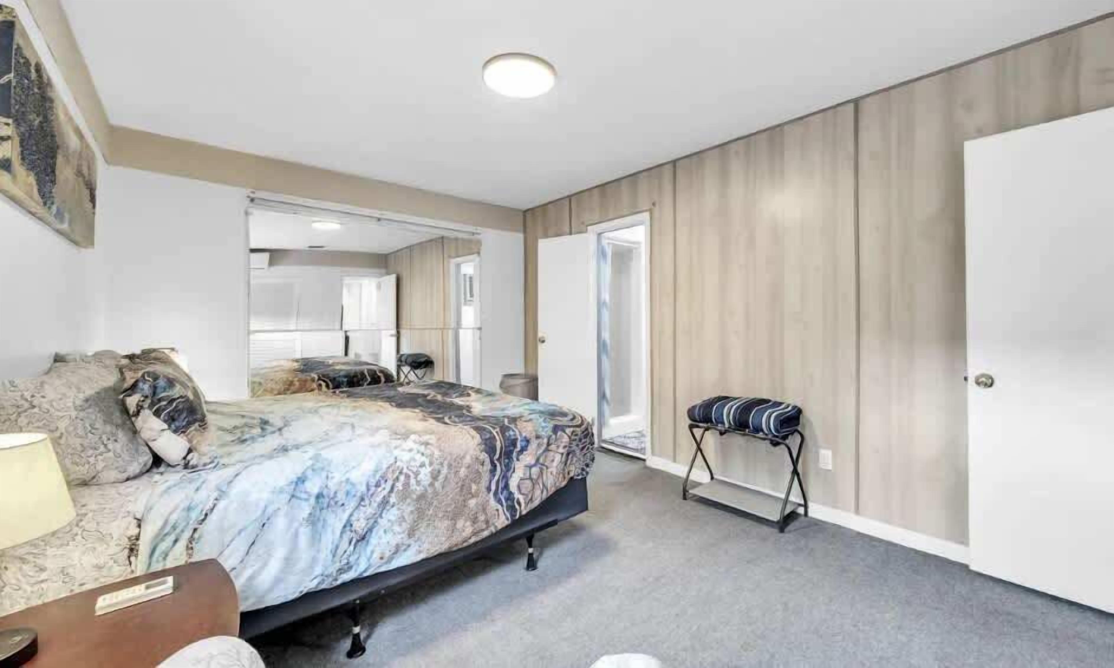 A bedroom with a bed, a bedside table, a lamp, a bench, and a wardrobe.