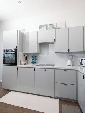 Una cocina moderna con armarios blancos, horno empotrado, licuadora y microondas.