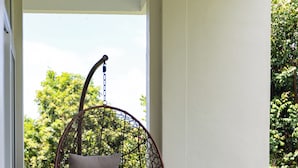 A hanging chair with a cushion on a balcony with a view of greenery.