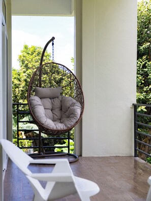 Una silla colgante con cojín en un balcón con vistas a la vegetación.