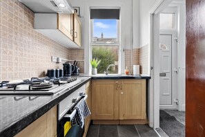 A kitchen with a gas stove, a sink, and wooden cabinets. - Spacious Leeds Home | Sleeps 6 | Free Parking (Beeston)