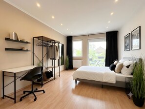 Ein modernes Schlafzimmer mit Bett, Schreibtisch, Stuhl und einem Balkon mit Aussicht.