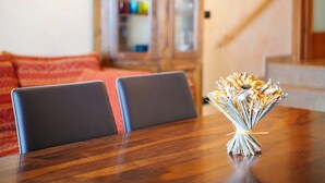 Una mesa de comedor con un ramo de flores secas en el centro, dos sillas y un aparador de madera al fondo.