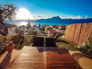 A patio with wooden flooring, a view of a coastal town, and a mountain in the background.