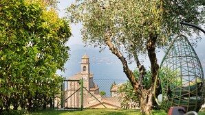 Vista de una iglesia con un campanario, rodeada de vegetación y una masa de agua.