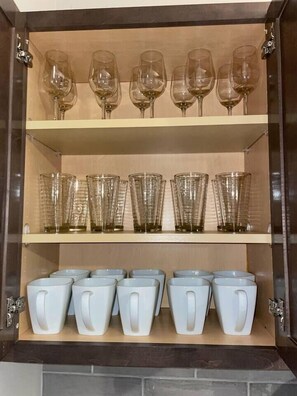 A cabinet with shelves containing wine glasses and mugs.
