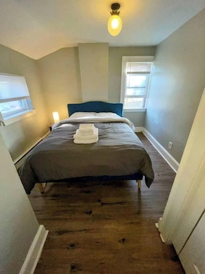 Une chambre à coucher avec un lit, une tête de lit, une fenêtre et un luminaire.