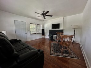 A living room with a black leather couch, a wooden dining table with chairs, a fireplace, and a ceiling fan.