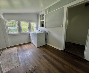 A laundry room with a washer and dryer, wooden flooring, and a view through a window.