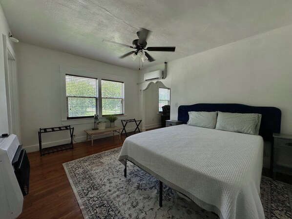 A bedroom with a bed, a ceiling fan, a desk with a chair, a window with blinds, and a radiator.