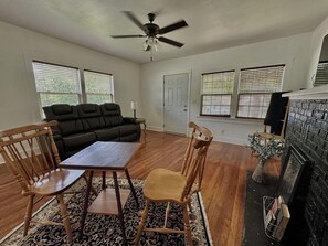 A living room with a sofa, two wooden chairs, a table, a ceiling fan, and a fireplace.