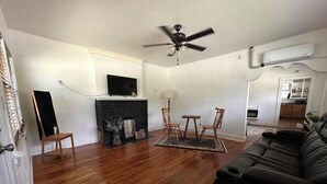 Uma sala de estar com lareira, ventilador de teto, televisão e sofá de couro preto.