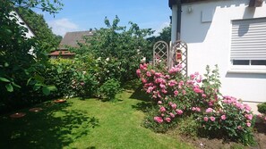 Ein Garten mit rosa Rosen, einem Holztor und einem weißen Gebäude.