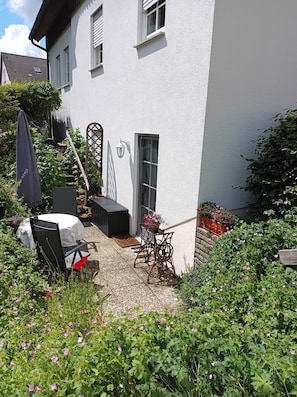 A white building with a door, windows, and a small garden area with a table and chairs.