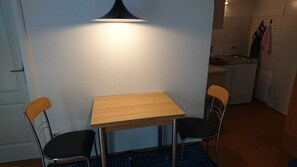 Ein kleiner Essbereich mit einem Holztisch und zwei Stühlen, einer schwarzen Pendelleuchte und einer Küche im Hintergrund.