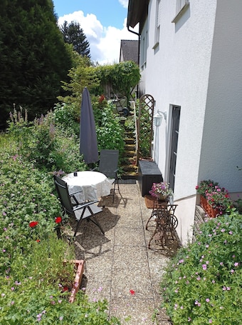 A patio with a table and chairs, surrounded by a garden with various plants and flowers.