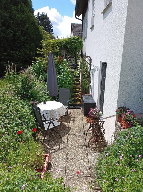 Eine Terrasse mit Tisch und Stühlen, umgeben von einem Garten mit verschiedenen Pflanzen und Blumen.