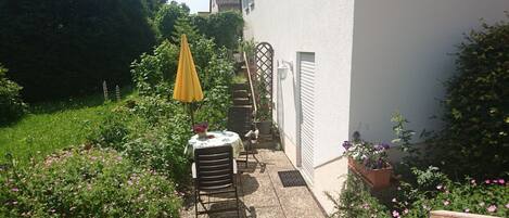 A garden patio with a table and chairs, surrounded by potted plants and flowers.
