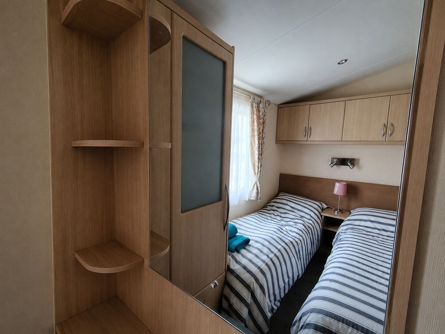 Quarto compacto com duas camas de solteiro, uma mesinha e um guarda-roupa com espelho.