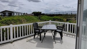 A deck with a white railing, two chairs, and a table. - Marine Holiday Park - 21nc (Rhyl)