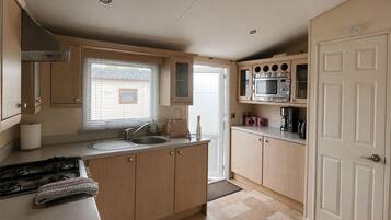 A compact kitchen with a gas stove, a sink, a microwave, and wooden cabinets.