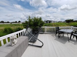 A deck with a white railing, a bench, a table with chairs, and a metal structure.