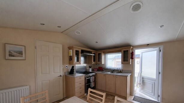 A compact kitchen with a dining table, chairs, a stove, and a sink. - Marine Holiday Park - 21nc (Rhyl)
