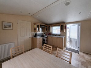 A compact kitchen with a dining table, chairs, a stove, and a sink. - Marine Holiday Park - 21nc (Rhyl)