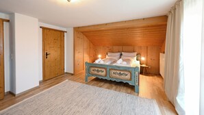 A bedroom with a wooden ceiling, a bed with decorative headboard, a bedside table with a lamp, and a door. - Alpenvilla Liboria Wallgau: 220-square-meter vacation home with hobby room (Wallgau)