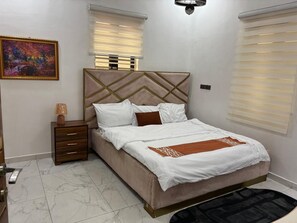 A bedroom with a bed, nightstands, a painting, and a chandelier. - Rossybella Residence (Lekki)