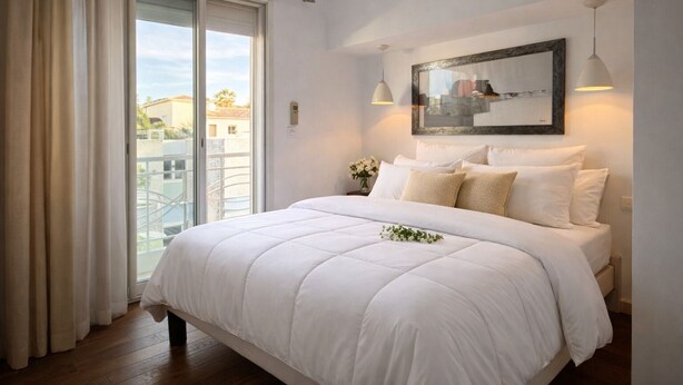 Een slaapkamer met een groot bed, een schuifpui naar een balkon, een ingelijste foto aan de muur en een hanglamp.