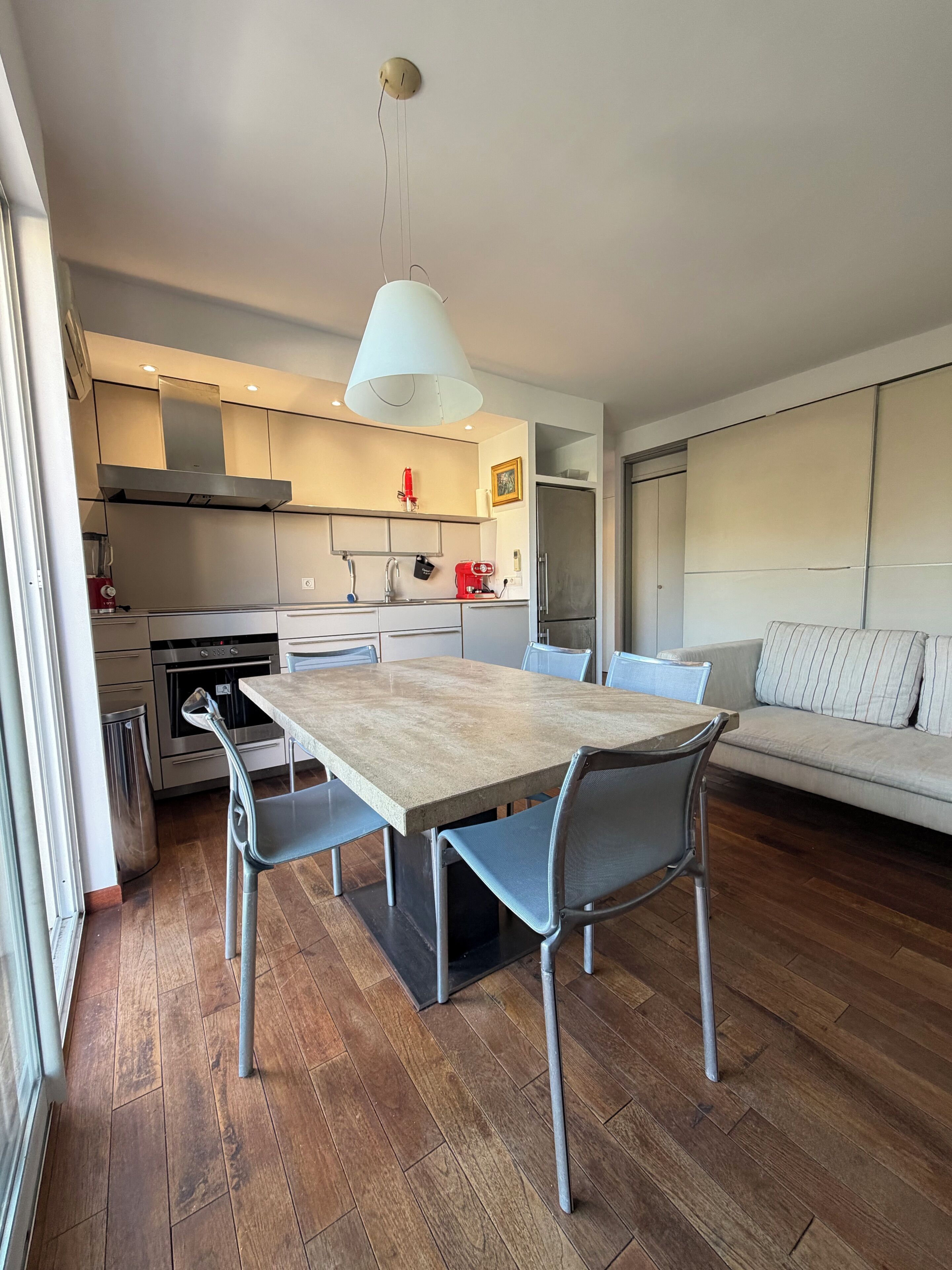 A modern kitchen with a dining table, chairs, and a hanging light fixture.