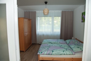 Ein Schlafzimmer mit einem Bett, einem Schrank, einem Fenster mit Vorhängen und einer Pendelleuchte.