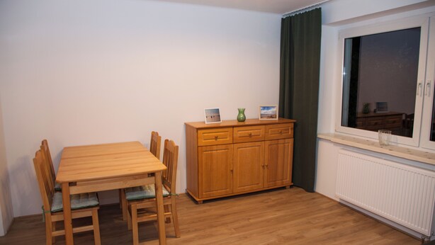A dining area with a wooden table and chairs, a wooden cabinet, and a window with curtains. - Apartment Joanna – 70 m² of comfort on Lake Turawa in Szczedrzyk, Poland (Upper Silesia) (Szczedrzyk)