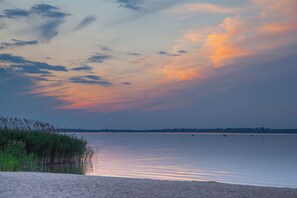 Ruhige Wasserfläche mit einer entfernten Küste, blauem Himmel und einigen Booten.