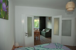 A room with a bed, a green sofa, a wooden chair, a dining table, and a window with curtains. - Apartment Joanna – 70 m² of comfort on Lake Turawa in Szczedrzyk, Poland (Upper Silesia) (Szczedrzyk)