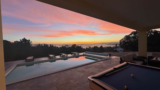 Ein Poolbereich mit Blick auf den Sonnenuntergang, Liegestühle und ein Billardtisch.