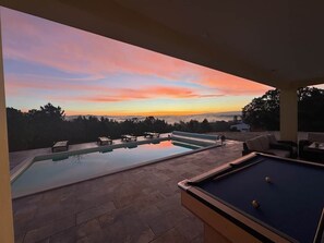 A pool area with a sunset view, lounge chairs, and a pool table.