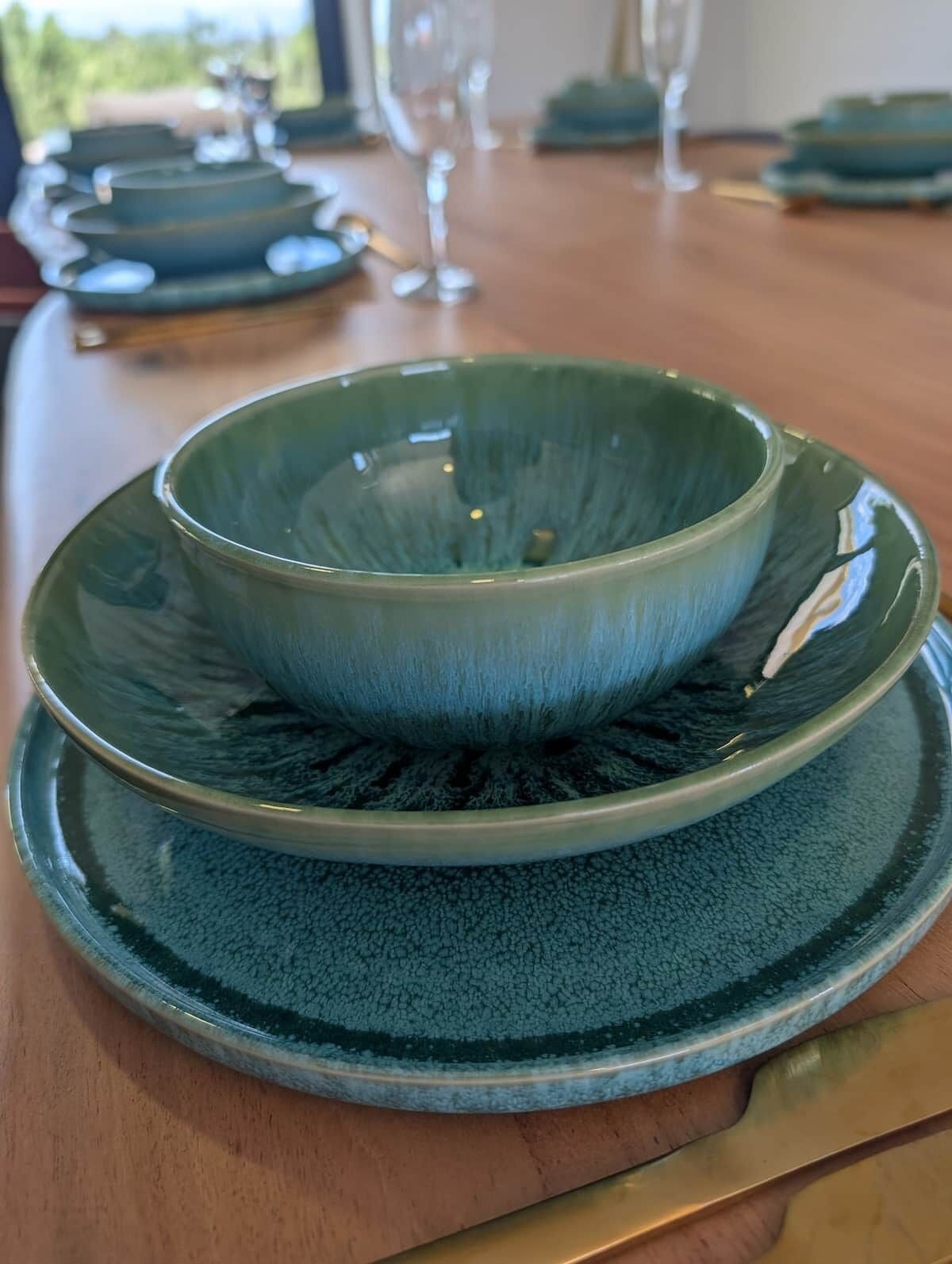 Uma mesa de jantar com um conjunto de pratos e tigelas de cerâmica verde.