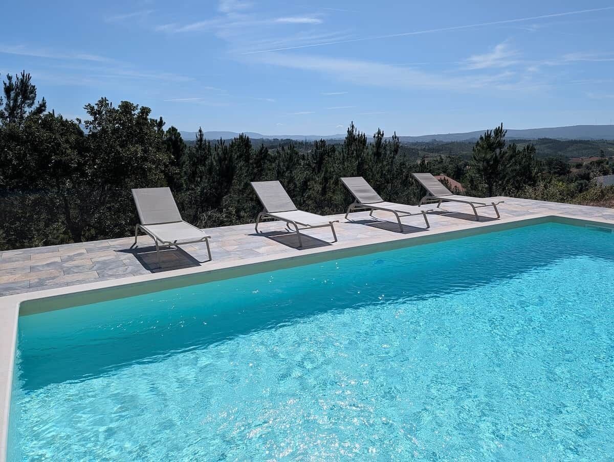 Une piscine rectangulaire à l’eau d’un bleu cristallin, entourée de chaises longues et bordée d’une terrasse en pierre.
