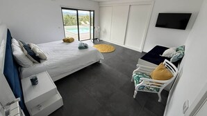 Ein modernes Schlafzimmer mit Bett, Sessel, Fernseher und Fenster.