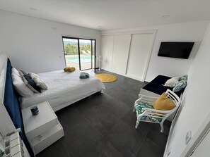 Ein modernes Schlafzimmer mit Bett, Sessel, Fernseher und Fenster.