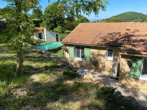 Une maison avec une piscine, des volets verts et un mur en pierre.