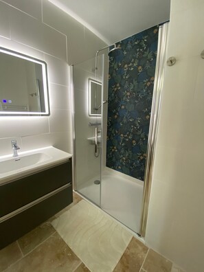 Casa de banho com cabine de chuveiro em vidro, lavatório com espelho e azulejos estampados.
