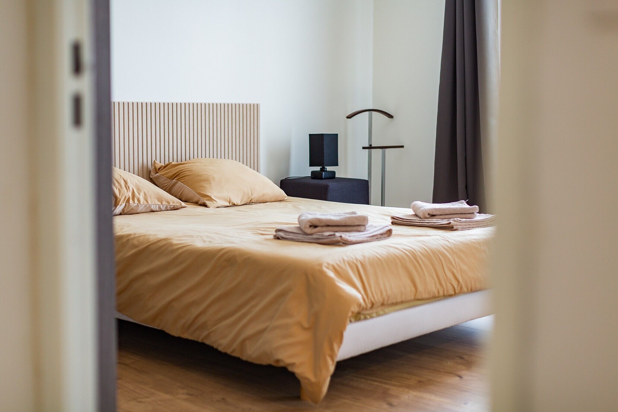 Un lit bien fait, avec une couvre-lit et des oreillers de couleur beige, une table de chevet avec une lampe et une lampe sur pied dans une chambre d’hôtel.