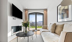 Ein modernes Wohnzimmer mit Flachbildfernseher, einer Couch, einem Couchtisch und einem großen Fenster mit Aussicht.