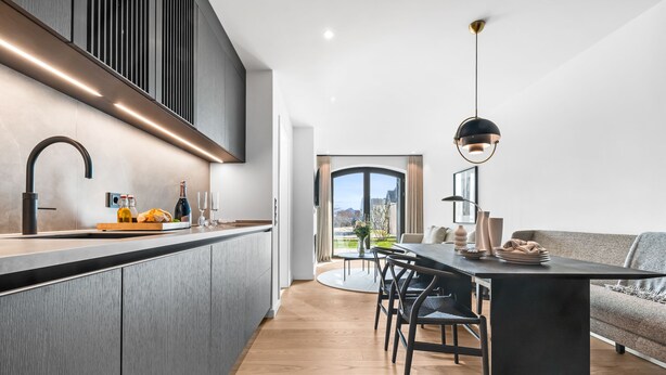 A modern kitchen with a central island, a dining area with a table and chairs, and a view of the outdoors through a large window. - Hudson Suite, a luxurious  featuring both a Finnish sauna and an infrared sauna. (List auf Sylt)