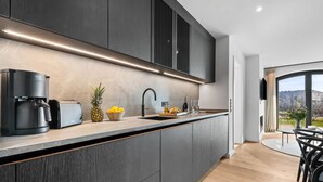A modern kitchen with dark cabinetry, a built-in coffee maker, a fruit bowl, and a view of the outdoors through a large window. - Hudson Suite, a luxurious  featuring both a Finnish sauna and an infrared sauna. (List auf Sylt)