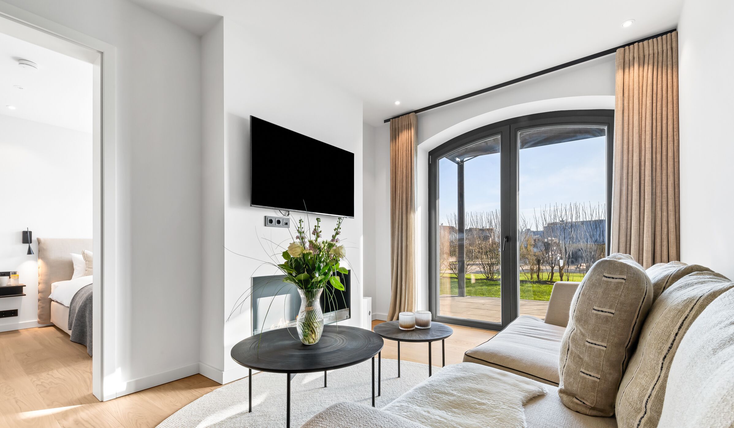 A modern living room with a large TV, a sofa, a coffee table, and a view of the outdoors.
